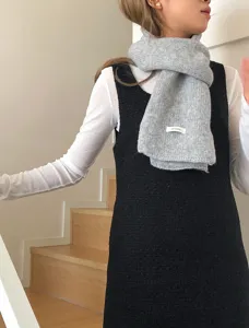 Close-up of a cozy grey knit scarf worn by a model indoors, showcasing soft winter texture.