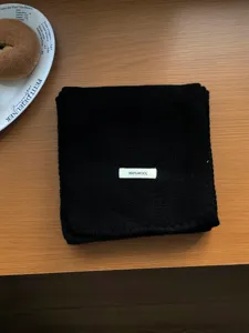 Black 100% wool scarf detail view, showing soft knitted texture and premium wool label.
