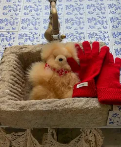 Vista detallada de guantes de lana tejidos en rojo con peluche en lavabo rústico de piedra.