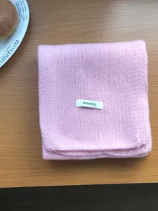 Close-up detail of a soft pink knitted wool scarf folded neatly on a wooden table.