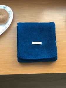 Detailed view of dark blue solid color wool knitted scarf folded neatly on a wooden table.
