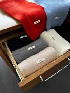 Close-up detail of soft 100% wool solid scarves neatly organized in a wooden drawer.
