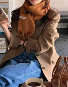 Primer plano de bufanda de lana lisa con flecos usada con blazer marrón en cafetería.