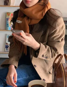 Detalle en primer plano de suave bufanda de lana marrón con flecos, portada con elegante estilo.