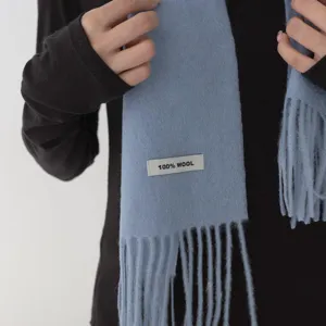 Primer plano de un pañuelo de flecos de lana azul claro suave con etiqueta de material.