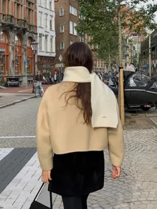 Detail shot of a soft white wool scarf worn with beige jacket in a European street style.
