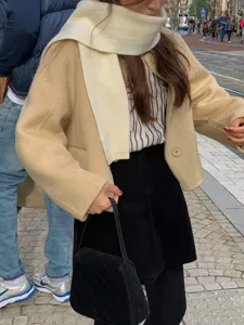 Cozy winter wool scarf styled with casual beige jacket and black corduroy skirt detail.