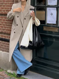 Detailed view of women's stylish winter long wool coat paired with denim jeans and black bag.