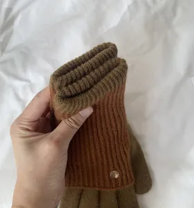 Close-up detail of warm knitted color block gloves featuring ribbed cuff and stylish metal button.