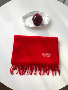 Detailansicht eines roten Wollschals mit besticktem Text und Fransen, weiche warme Textur.