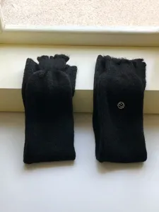 Detail van zwarte gebreide beenwarmers met zachte woltextuur en een klein metalen hartlogo.