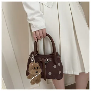 Detailopname van bruine polkadot emmertas met schattige pluche hond bedel en riemgesp accent.