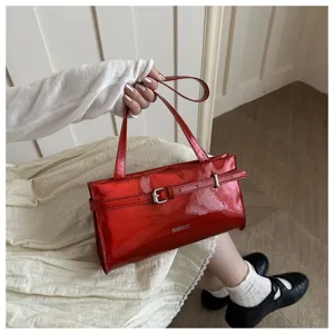 Close-up detail of stylish red patent leather shoulder bag with chic metal buckle decoration.