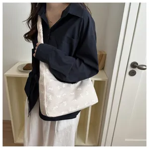 Close-up detail of beige checkered shoulder bag with cute bow embroidery worn by model.