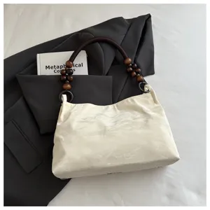 Borsa a mano chic in tessuto bianco sporco con manico di perle in legno e blazer scuro.