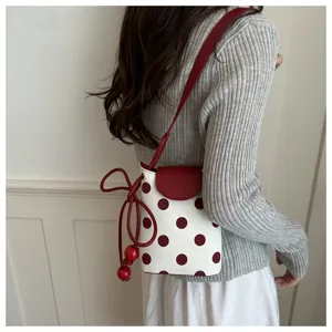 Primo piano di una elegante borsa a tracolla bianca a pois con patta e tracolla rosse.