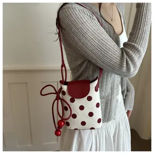 Primo piano dettaglio della borsa a tracolla da donna a pois con patta rossa e decoro perle.