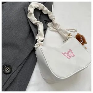 Dettaglio della borsa a spalla bianca con tracolla arricciata e ricamo di farfalla rosa.