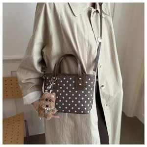 Nahaufnahme einer braunen Schulter-Eimer Tasche mit Punkten und flauschigem Welpen-Anhänger.