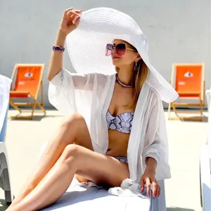 Oversized white straw beach hat detail shot, wide brim sun protection vacation summer style.