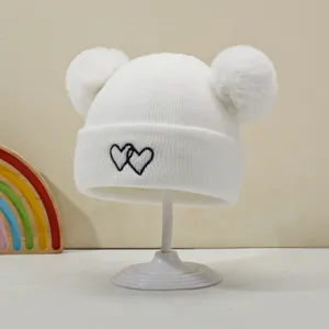 White baby knit beanie with double pom poms and cute heart embroidery for warm winter wear.