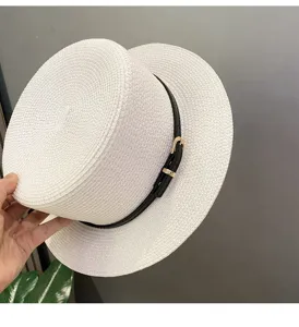 Close-up detail of a white straw boater hat featuring a black belt and sleek gold buckle.