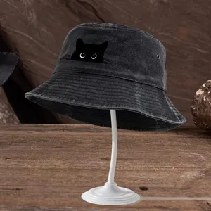 Gros plan du chapeau bob en jean noir avec motif de chat sur un support en bois.