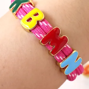 Close-up detail of colorful enamel letter charms on the pink braided rope bracelet design.