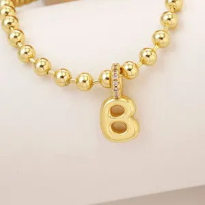Close-up detail shot of a gold-plated bubble letter charm pendant on a matching bead chain necklace.