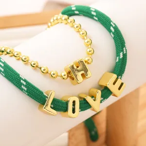 Set de pulsera de cuerda verde tejida y cadena dorada con abalorios de letras brillantes.