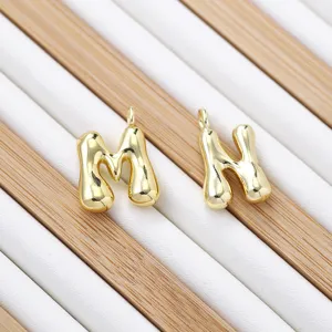 Detail view of cute 3D gold puffy letter M and N charms, shiny polished metal jewelry pendant.