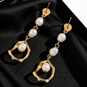 Close-up detail of elegant gold drop earrings with pearls on black silk texture background.