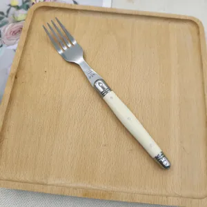 Detail view of ivory white handle Laguiole style stainless steel steak fork on wooden tray