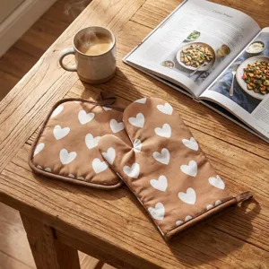 Close-up of thick oven mitt and pot holder set with white heart pattern on wooden table.