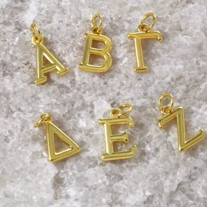 Détail en gros plan de pendentifs lettres grecques plaquées or, idéal pour la bijouterie DIY.