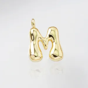 Close-up detail of a shiny gold puffed letter M pendant, featuring a smooth 3D curved design.