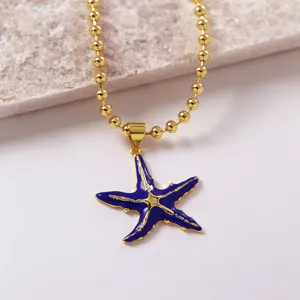 Collana di perle dorata con ciondolo stella marina in smalto blu scuro, dettaglio di gioielli.