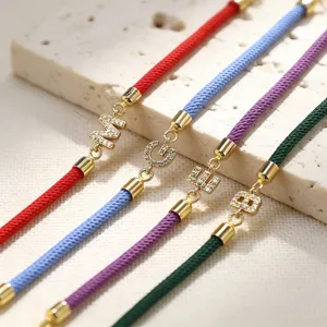 Primo piano dettagliato di bracciali intrecciati in corda colorata con ciondoli lettere in zircone.