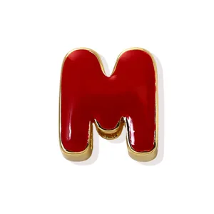 Close-up detail of a red enamel gold plated letter M charm pendant, elegant craft and glossy finish.