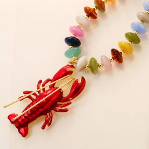 Gros plan détaillé du pendentif homard rouge vif associé à un collier de perles acryliques.