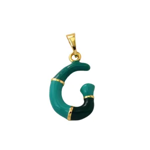 Detail shot of letter G pendant with green and black enamel on shiny gold-plated brass metal.
