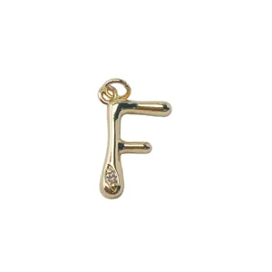 Close-up detail of a gold letter F pendant with a tiny sparkly crystal charm accessory.