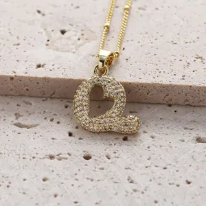 Gros plan détaillé d'un pendentif lettre Q dorée avec oxydes de zirconium sur fond en pierre.