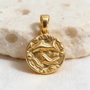 Detailed close-up of a vintage gold-plated coin pendant featuring an intricate dolphin relief design.