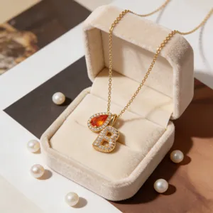 Detailopname van een vergulde letter B en geboortesteen hanger ketting in fluwelen doosje.