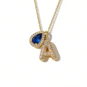 Vergulde ketting detail met blauwe druppelvormige edelsteen en kristallen letter A hanger.