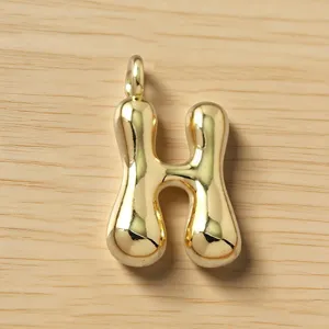 Detalle de colgante con letra H dorada inflada, accesorio de joyería de metal con estilo burbuja.
