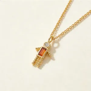 Detalle de un colgante de robot chapado en oro con circonita naranja y piedra clara en la cabeza.