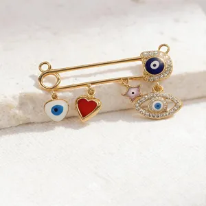 Gold evil eye safety pin pendant detail, featuring enamel charms and sparkling rhinestones.