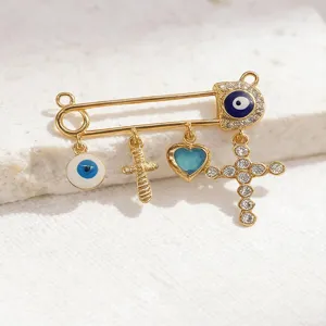 Close-up detail view of the retro gold safety pin brooch featuring evil eye charms and cross.